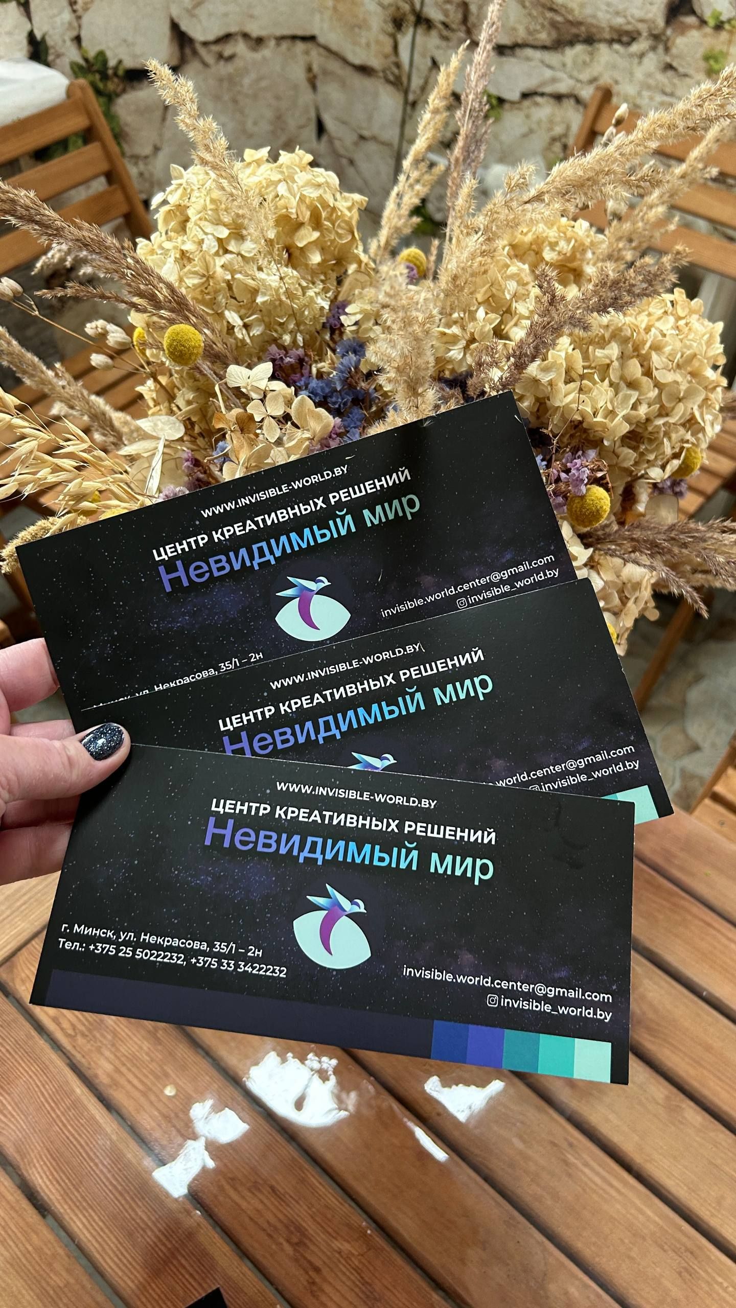 Подарочные сертификаты «Невидимый мир» в руке на фоне сухоцветов